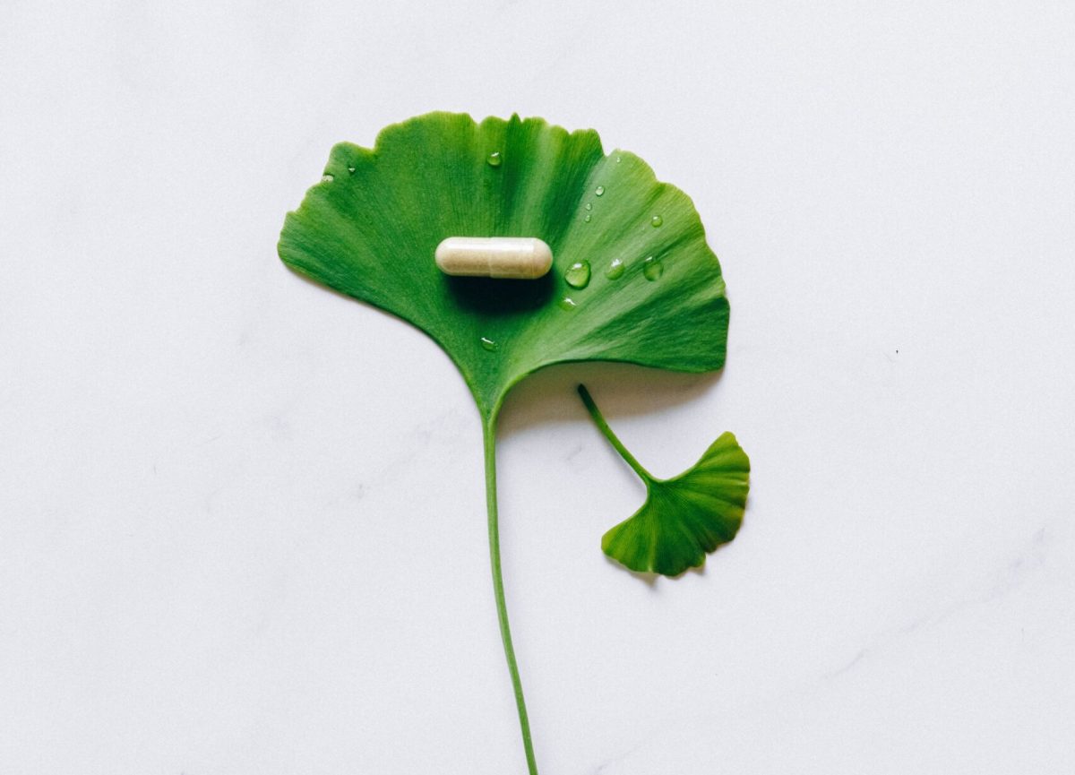 A ginkgo leaf with a water droplet covered supplement pill on a marble surface